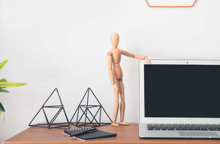 Wooden mannequin with laptop and stationery on table in office