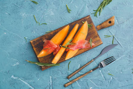 Board with delicious melon and prosciutto on color backgroundの写真素材