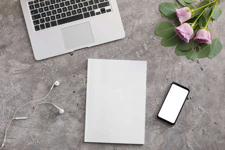 Blank magazine, laptop, mobile phone and flowers on gray background