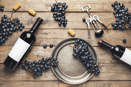 Bottles of red wine with fresh grapes and corkscrew on wooden background