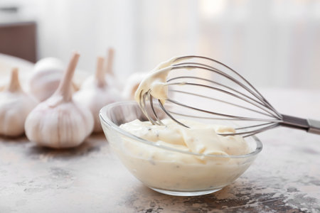 Bowl with garlic sauce and whisk on tableの写真素材