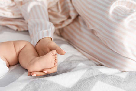 Mother holding foot of her little baby on bed at homeの写真素材