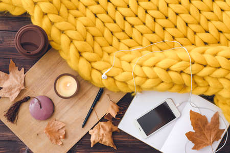 Autumn composition with knitted plaid, book and mobile phone on tableの写真素材