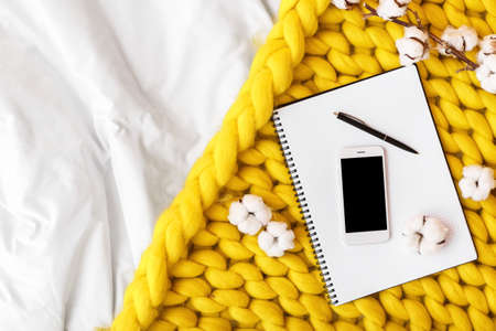 Mobile phone with notebook and knitted plaid on bedの写真素材