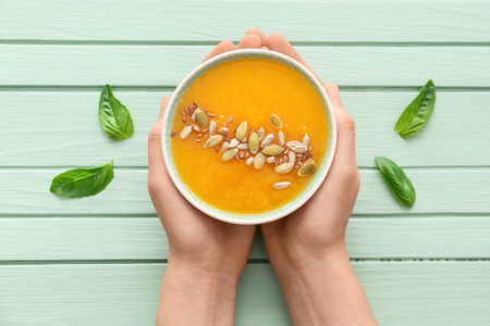 Female hands with tasty pumpkin cream soup in bowl on wooden backgroundの写真素材