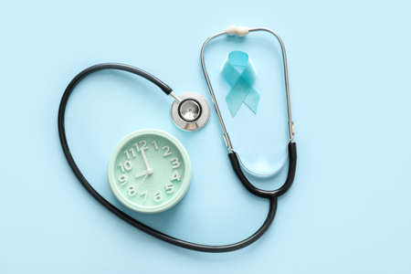 Blue ribbon, alarm clock and stethoscope on color background. Prostate cancer awareness conceptの写真素材