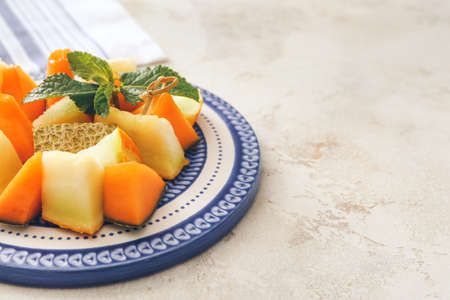 Plate with sweet cut melon on light background