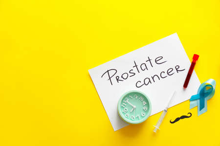 Paper sheet with text PROSTATE CANCER, clock, ribbon, mustache, syringe and blood sample on color...