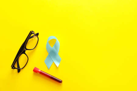 Blue ribbon, eyeglasses and blood sample on color background. Prostate cancer awareness concept
