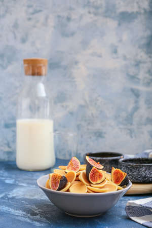Bowl with tasty pancakes, figs and milk on color background
