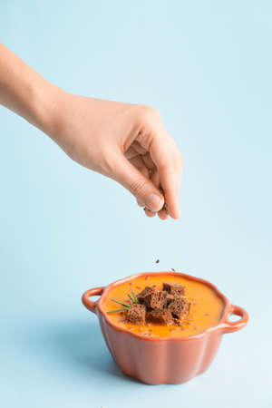 Woman cooking tasty pumpkin cream soup on color background