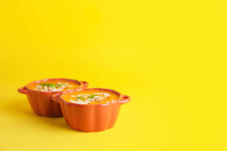 Tasty pumpkin cream soup in pots on color backgroundの写真素材