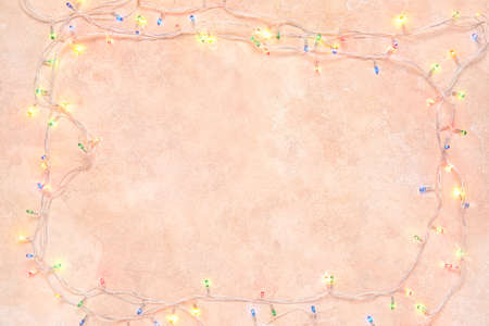 Frame made of Christmas lights on color background