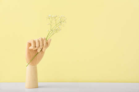 Wooden hand with flowers on color background