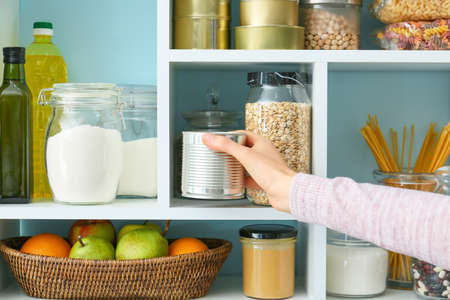 Woman taking metal can from shelves with products in kitchenの写真素材