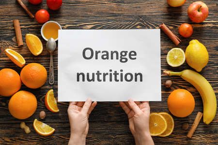 Female hands with text ORANGE NUTRITION on paper sheet and fresh products on wooden backgroundの写真素材