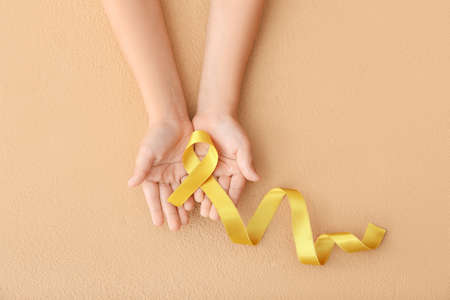 Child's hands with golden ribbon on color background. Cancer awareness conceptの写真素材