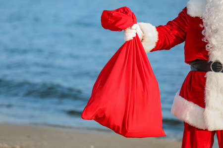 Santa Claus with Christmas gifts in bag on beachの写真素材