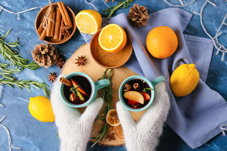 Female hands with cups of tasty mulled wine on color backgroundの写真素材
