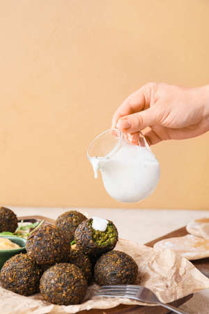 Woman pouring sauce onto falafel balls on color background