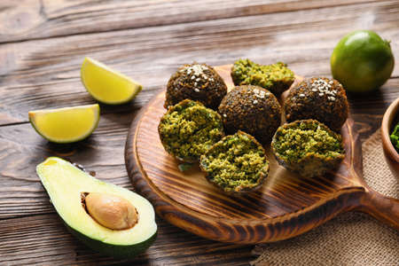 Board with tasty falafel balls, avocado and lime on wooden background