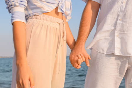 Happy young couple holding hands on sea beach, closeup