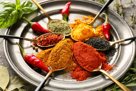 Spoons with different spices on dark background, closeup