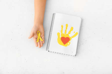 Hand with golden ribbon and notebook on white background. Childhood cancer awareness conceptの写真素材