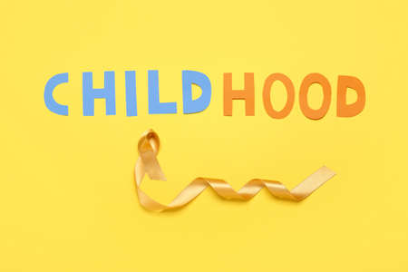 Golden ribbon and word CHILDHOOD on color background. Cancer awareness conceptの写真素材
