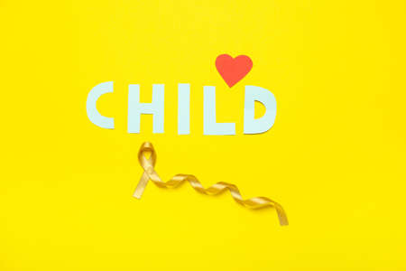 Golden ribbon, word CHILD and red heart on color background. Childhood cancer awareness conceptの写真素材