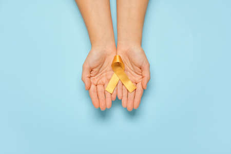 Hands with golden ribbon on color background. Childhood cancer awareness conceptの写真素材