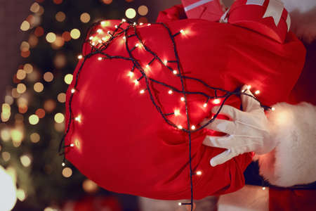 Santa Claus with bag full of Christmas gifts in room at nightの写真素材