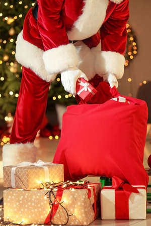 Santa Claus with bag full of Christmas gifts in room at nightの写真素材