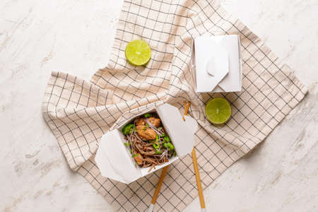 Container with tasty soba noodles and meat on light background
