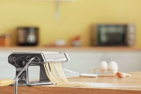 Pasta maker with dough on table in kitchenの写真素材