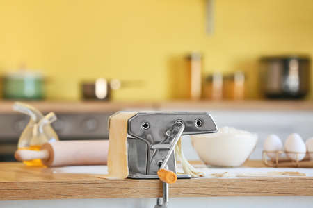 Pasta maker with dough on table in kitchen