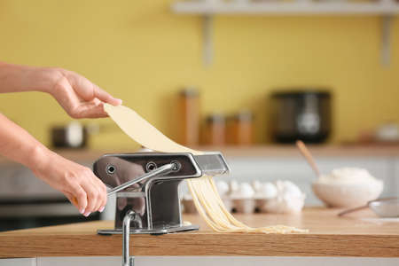 Woman making pasta with machine on table in kitchenの写真素材