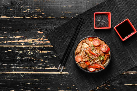 Plate with tasty noodles and meat on dark wooden background