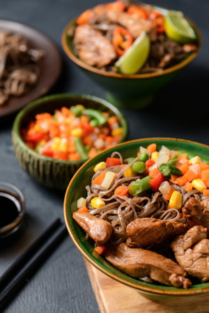 Bowls with tasty soba noodles, vegetables and meat on dark background, closeupの写真素材