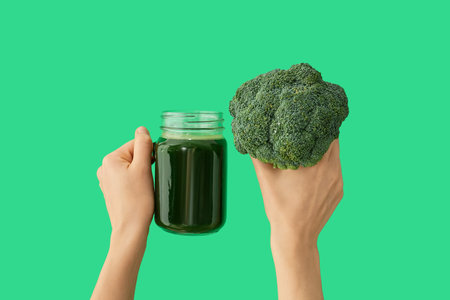 Hands with mason jar of broccoli juice on color backgroundの写真素材
