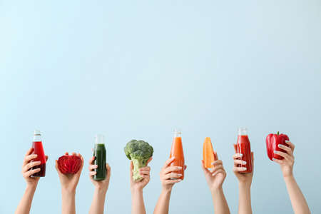 Many hands with bottles of vegetable juices on color backgroundの写真素材