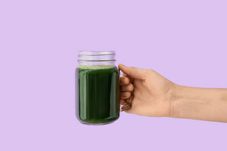 Hand with mason jar of vegetable juice on color backgroundの写真素材