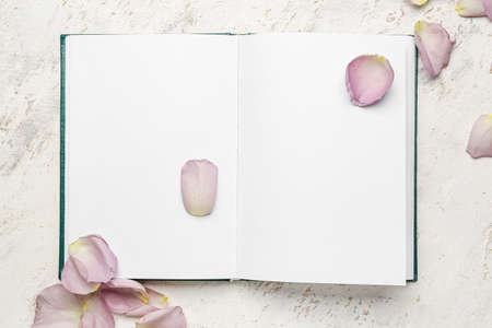 Blank book with rose petals on white background
