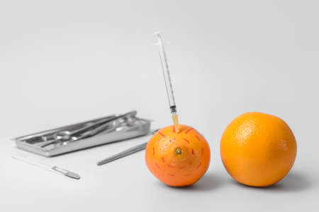 Fresh oranges with syringe and surgical tools on light background. Breast augmentation concept