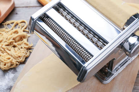 Pasta machine with dough on wooden background