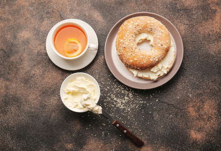 Bagel with tasty cream cheese and cup of tea on grunge backgroundの写真素材