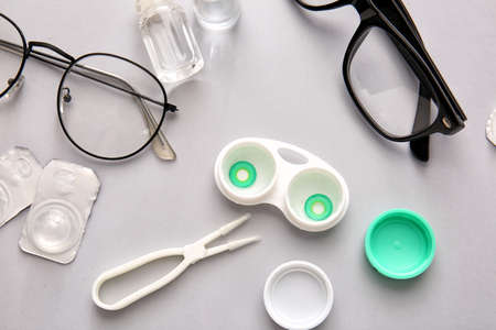 Eyeglasses, tweezers and container with contact lenses on light background