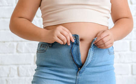 Overweight girl in tight clothes on white brick background, closeup