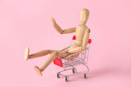 Wooden mannequin in shopping cart on color backgroundの写真素材