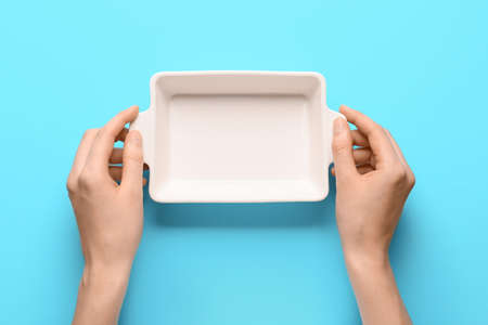 Female hands with baking dish on color backgroundの写真素材